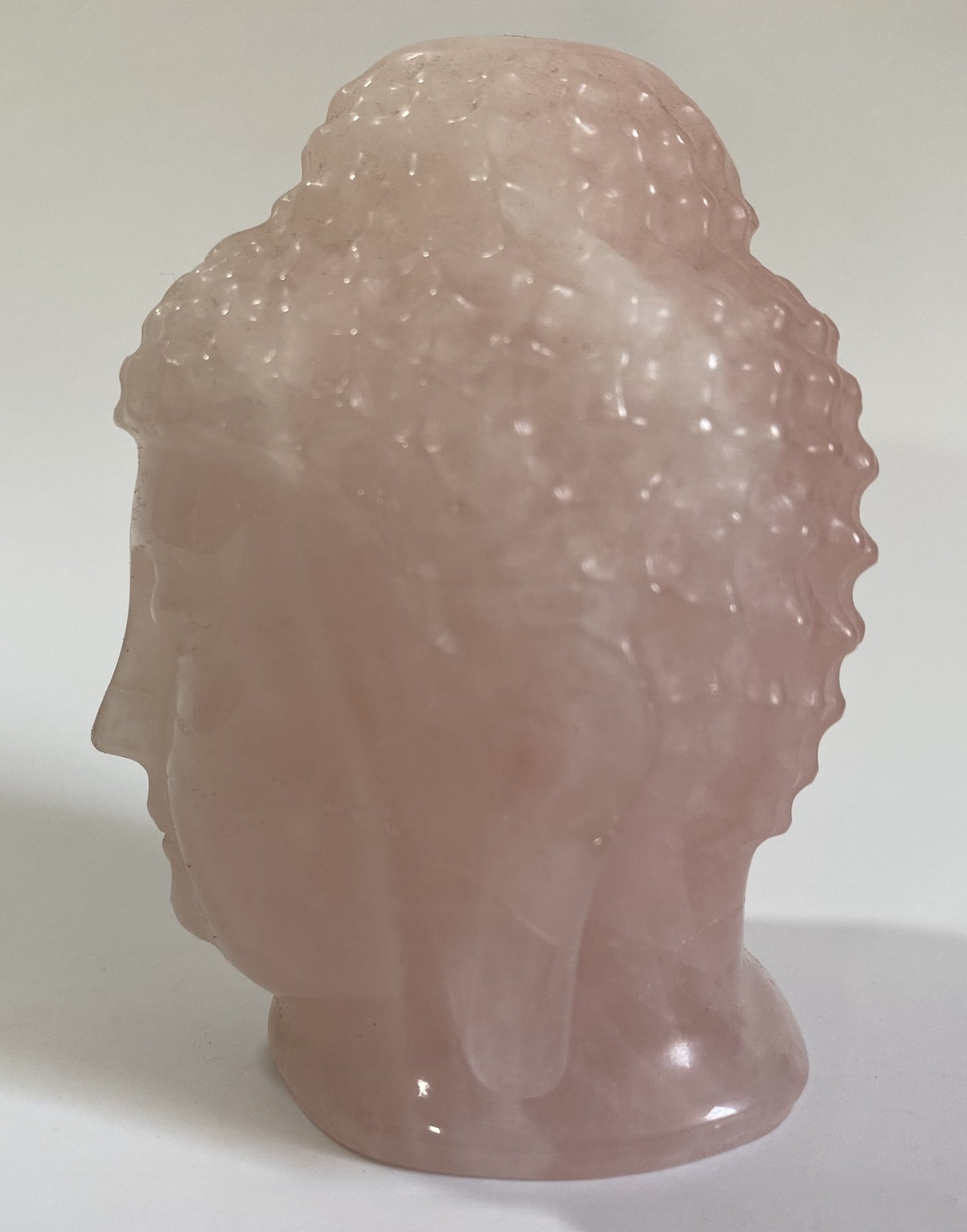 Sculptura Buddha din cuart roz pe fond alb sub lumina naturala