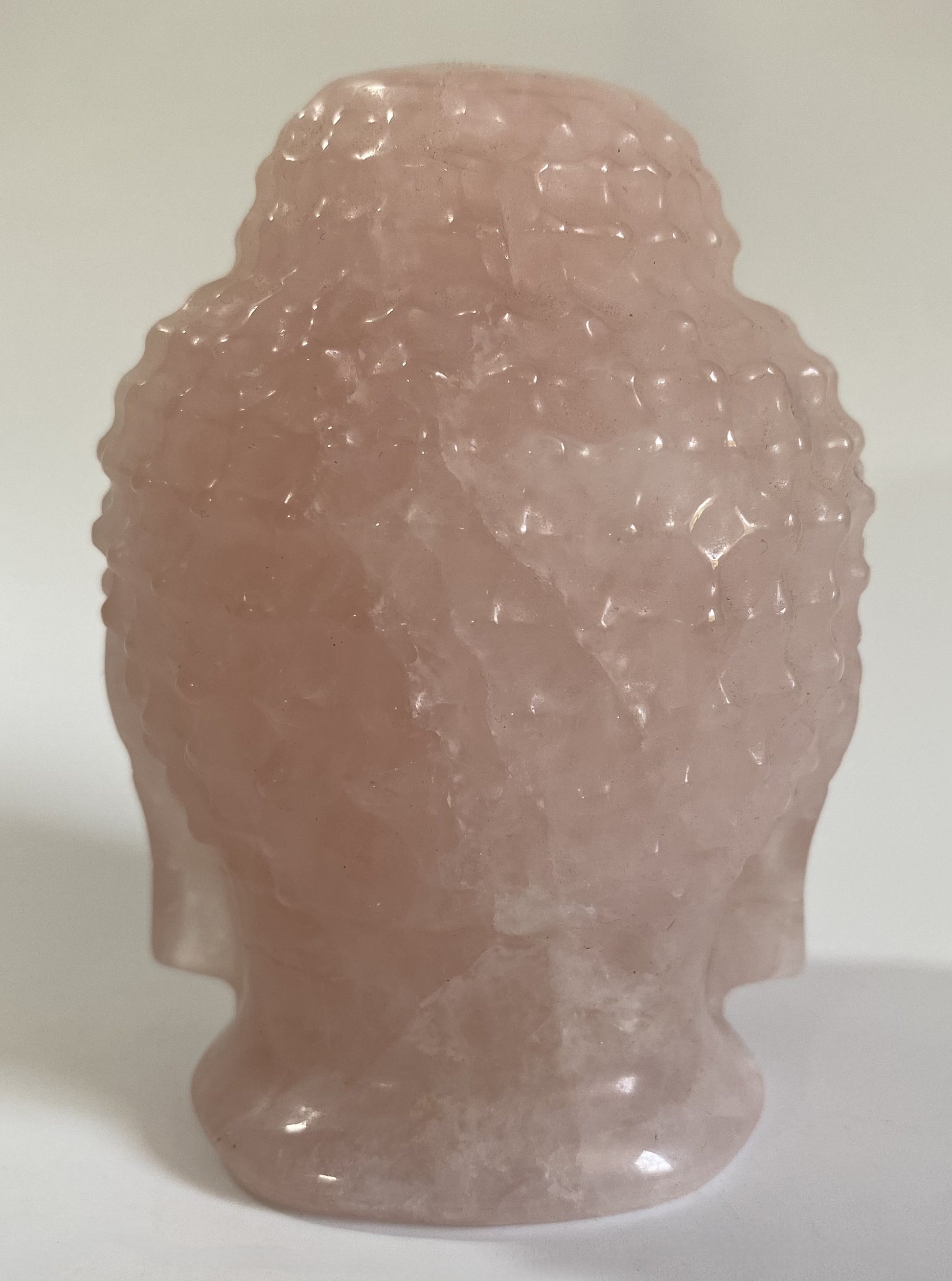 Sculptura Buddha din cuart roz pe fond alb sub lumina naturala