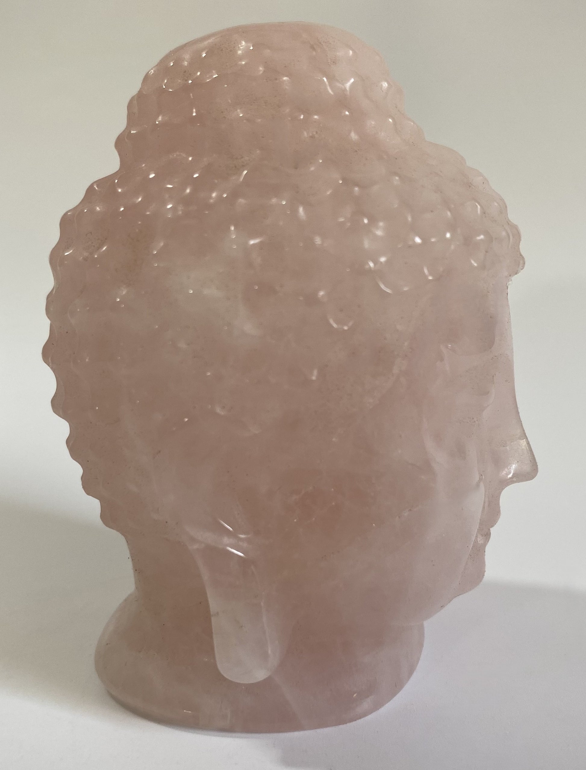 Sculptura Buddha din cuart roz pe fond alb sub lumina naturala