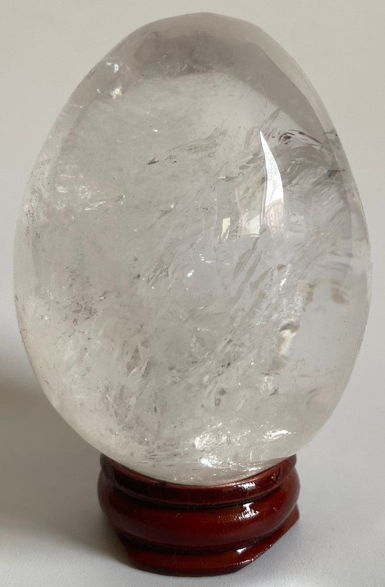 Ou yoni de 6.4cm din piatra semipretioasa de cuart transparent pe suport din lemn cu fundal alb