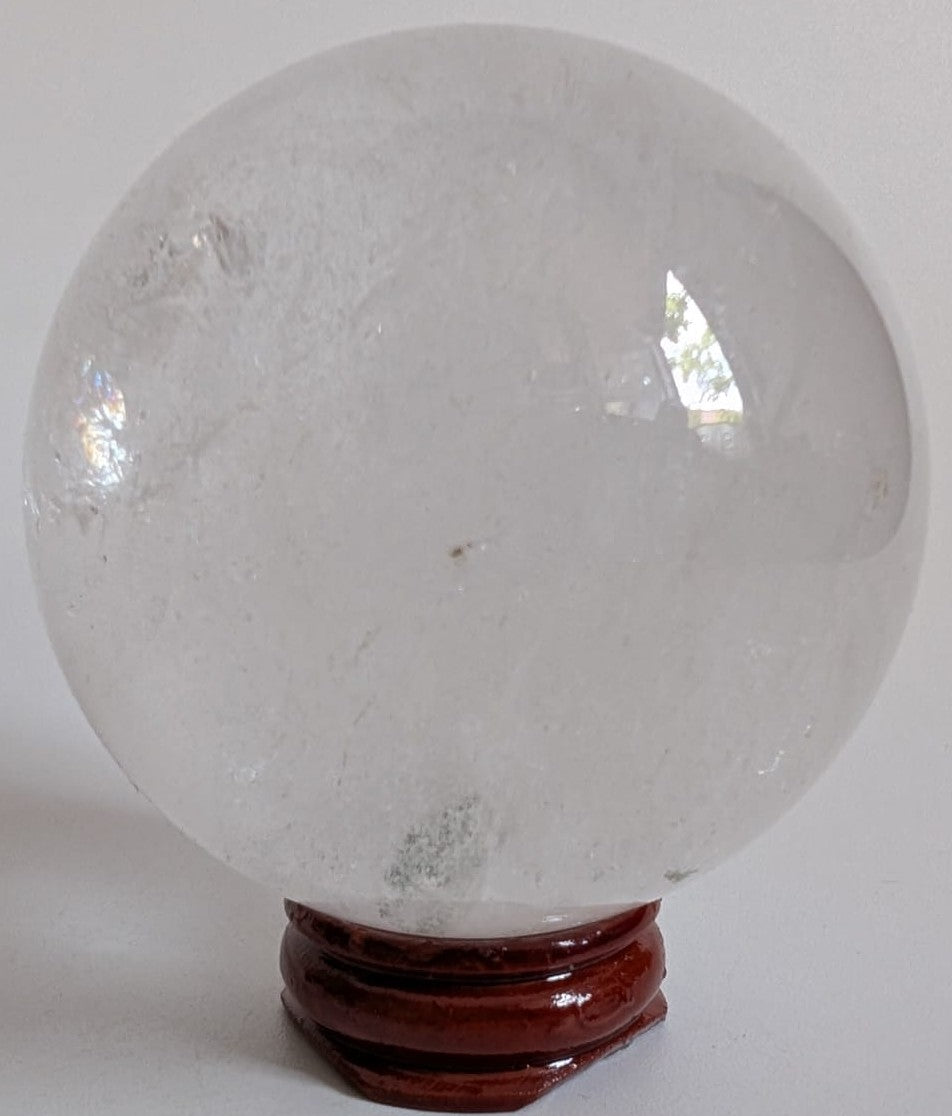 Sfera din piatra semipretioasa de cuart transparent pe suport din lemn cu fundal alb
