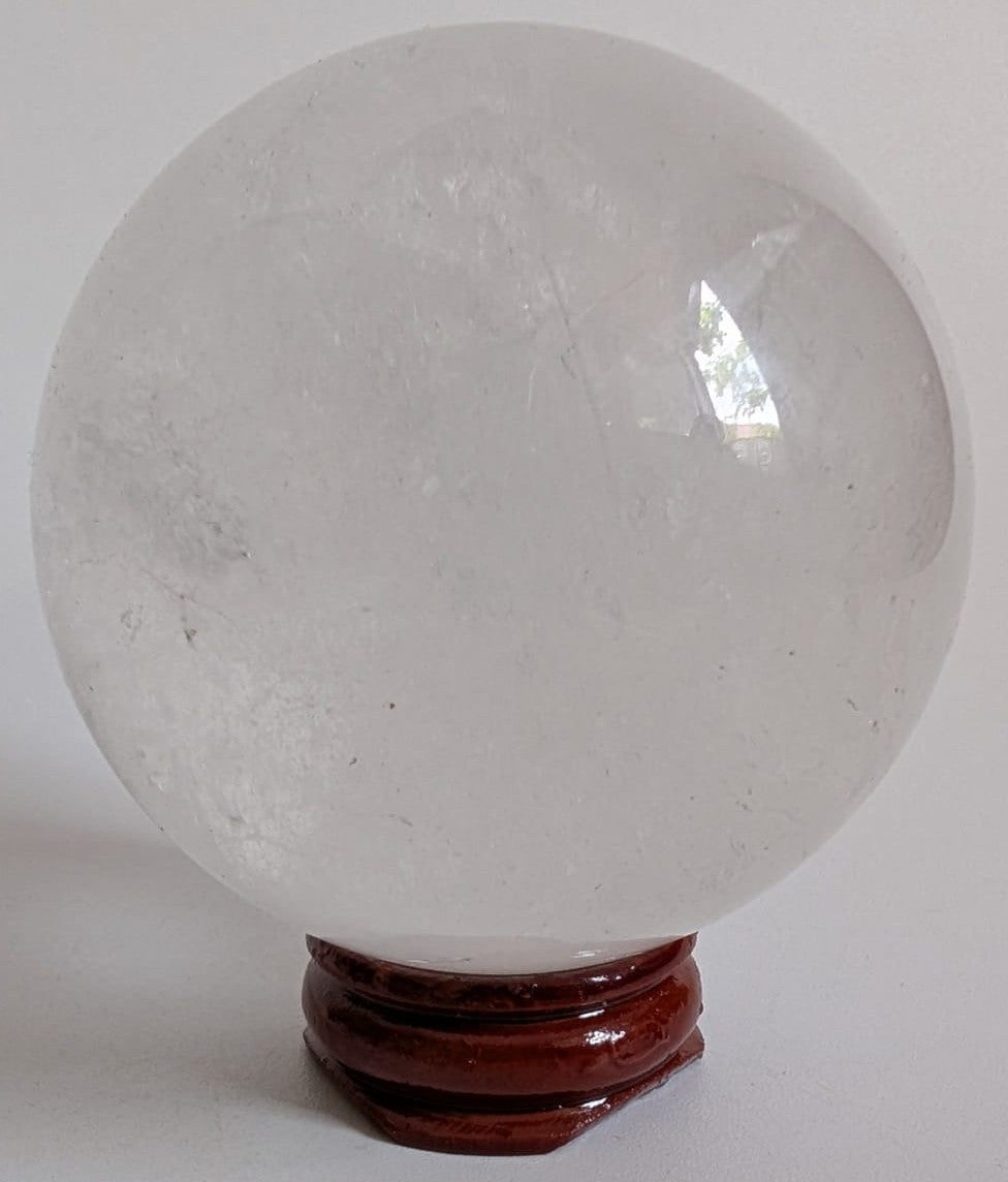 Sfera de 6.2cm din piatra semipretioasa de cuart transparent pe suport din lemn cu fundal alb