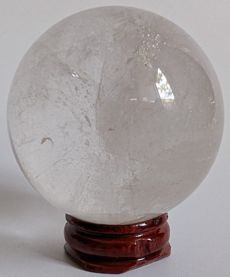 Sfera din piatra semipretioasa de cuart transparent pe suport din lemn cu fundal alb