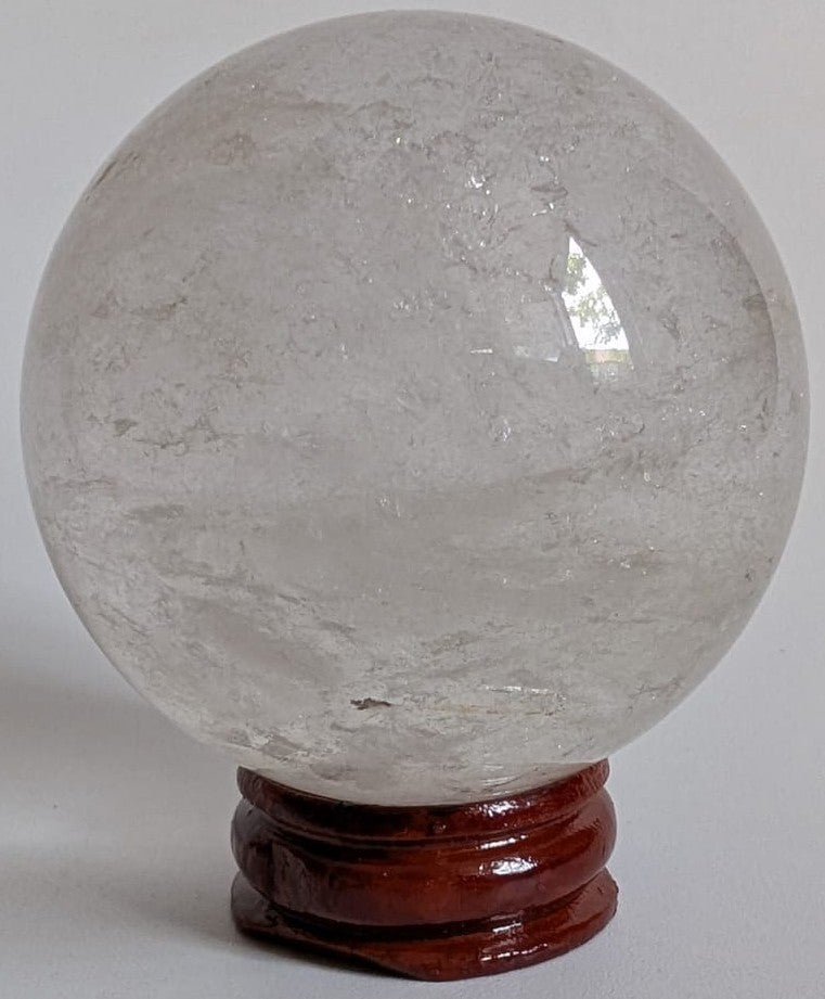 Sfera din cristal de cuart transparent pe suport din lemn cu fundal alb