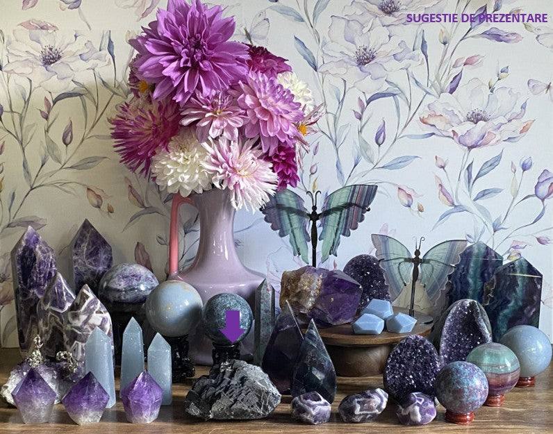 Specimen de Fluorit Black Rose printre cristale decorative și flori mov într-un aranjament de colecție minerală naturală