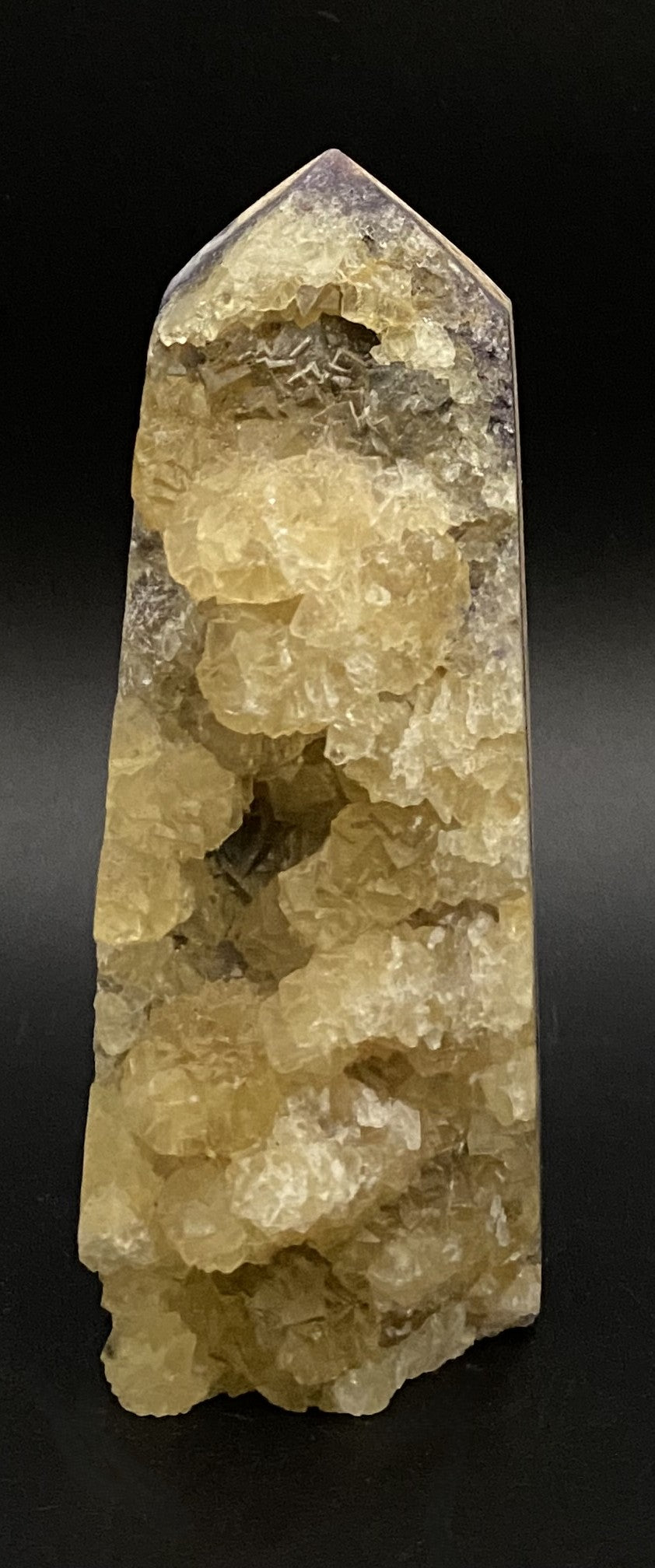 Obelisc brut din cristal de fluorit galben pe fundal negru sub lumina artificiala