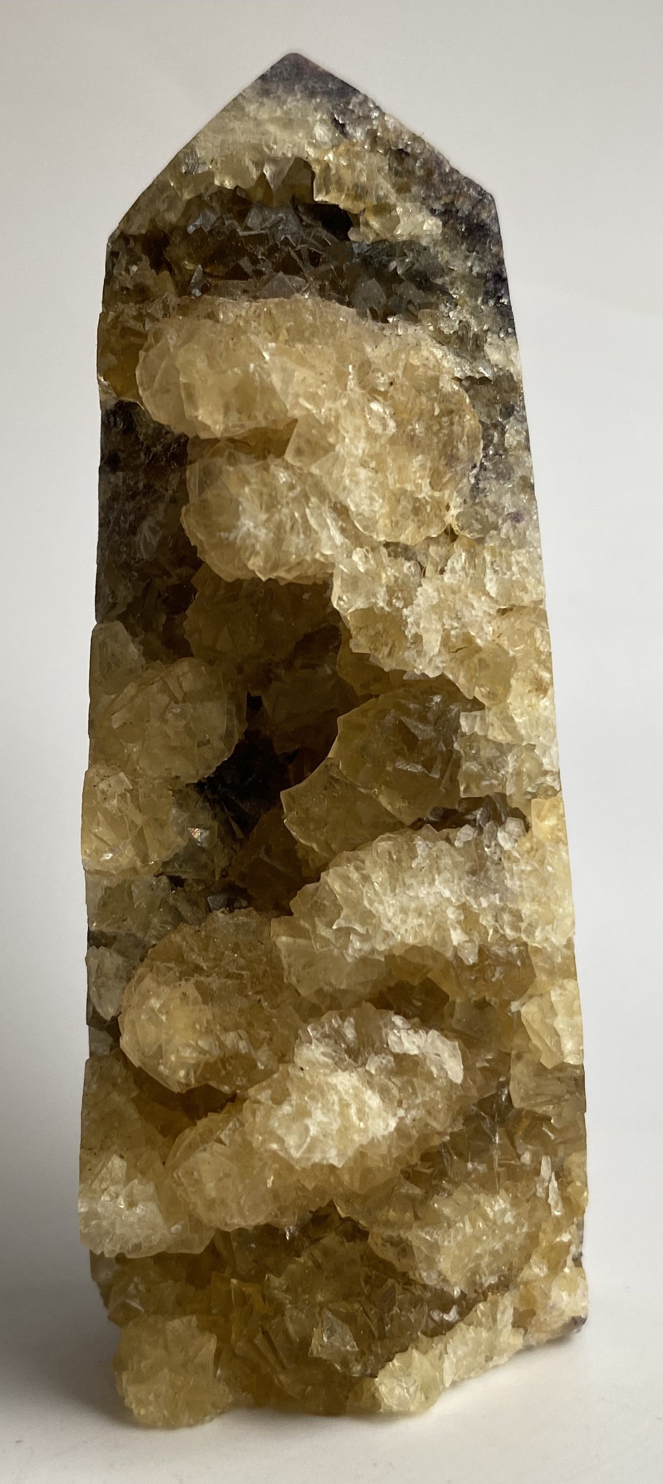 Obelisc brut din cristal de fluorit galben pe fundal alb sub lumina naturala
