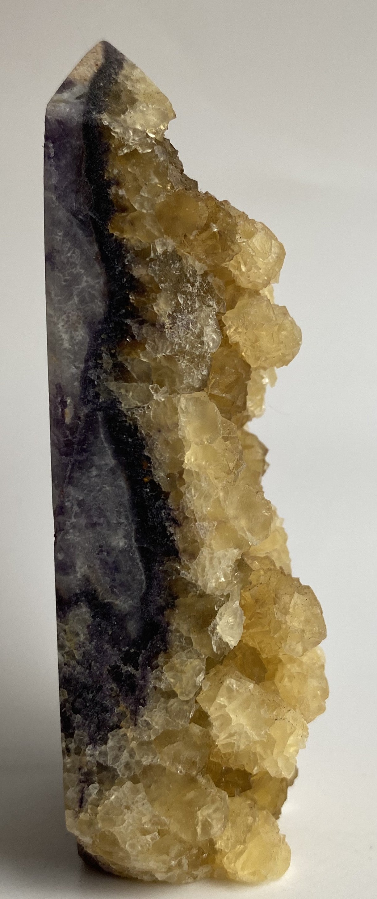 Obelisc brut din cristal de fluorit galben pe fundal alb sub lumina naturala