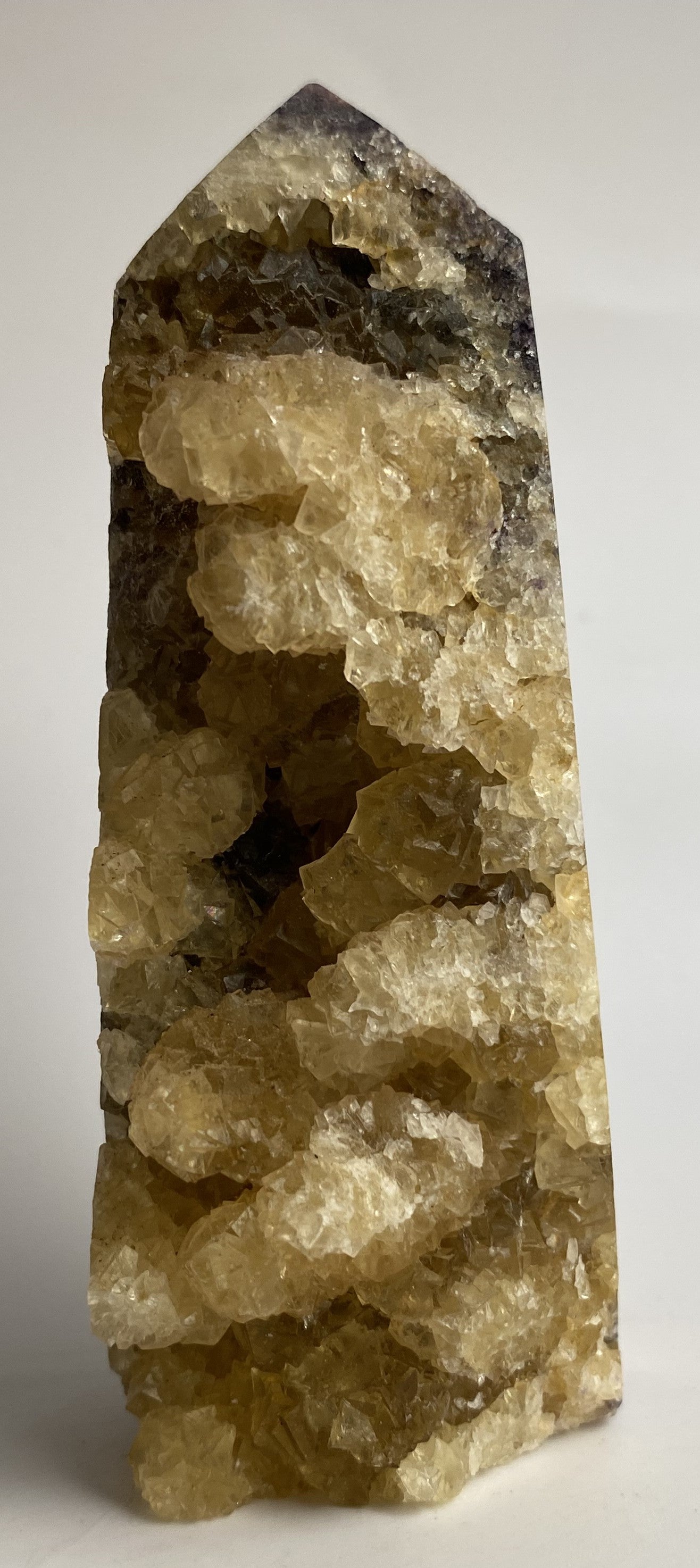 Obelisc brut din cristal de fluorit galben pe fundal alb sub lumina naturala