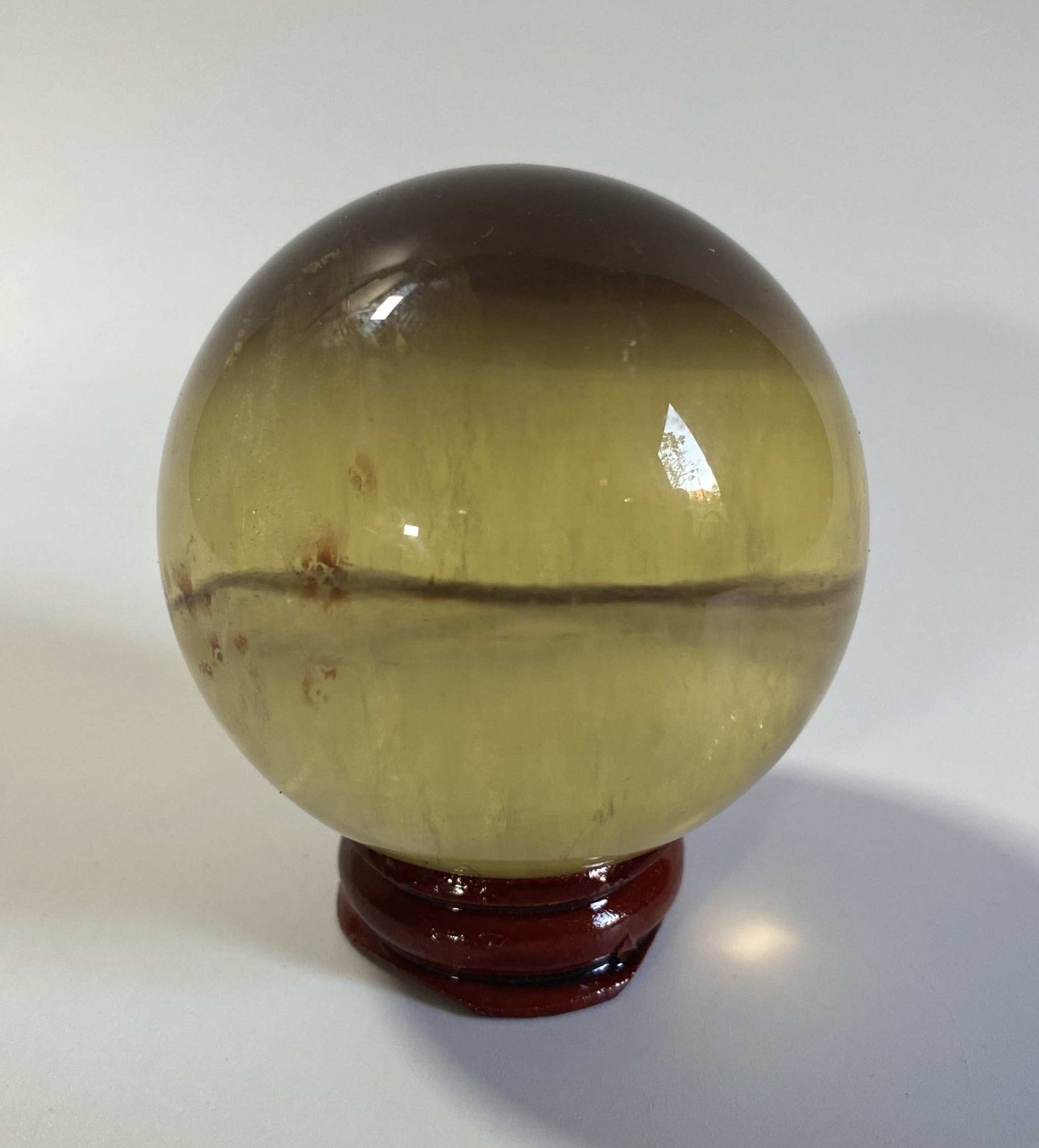 Sfera din fluorit galben semi-transparent pe suport lemn