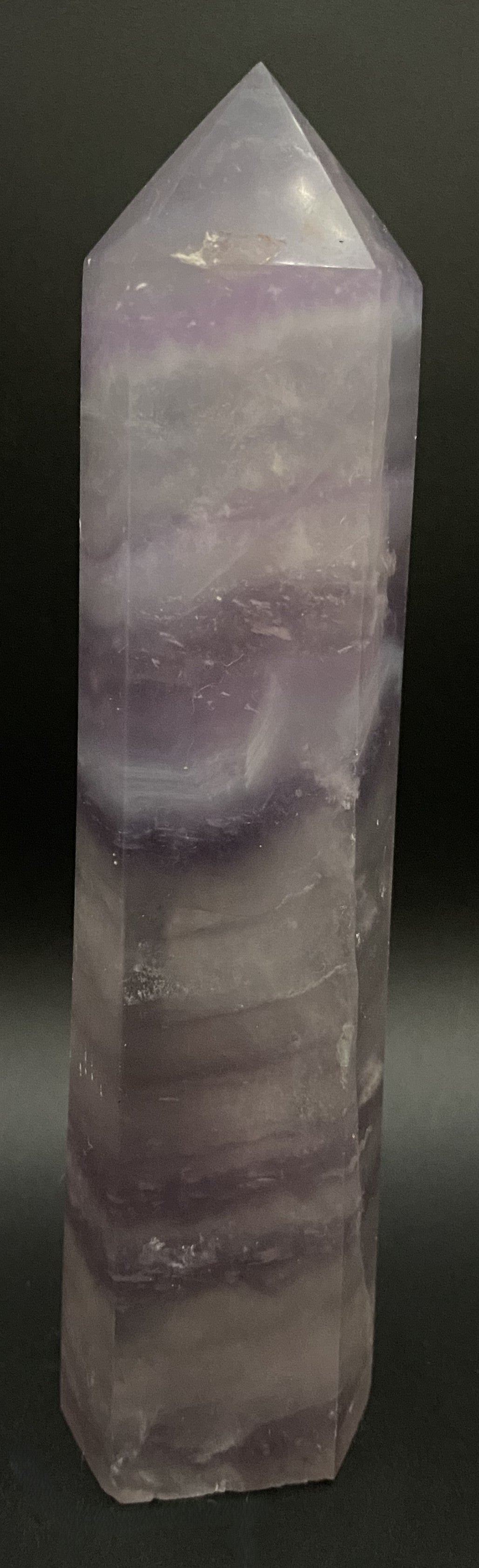 Obelisc din cristal de fluorit mov pe fundal negru sub lumina artificiala