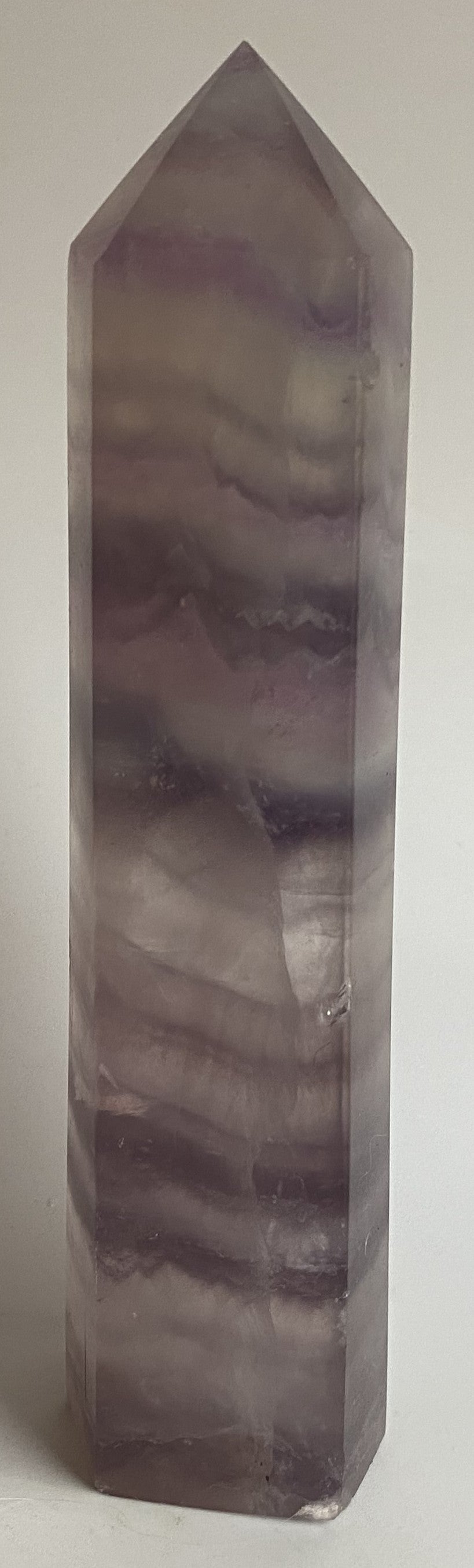 Obelisc din cristal de fluorit mov pe fundal alb sub lumina naturala