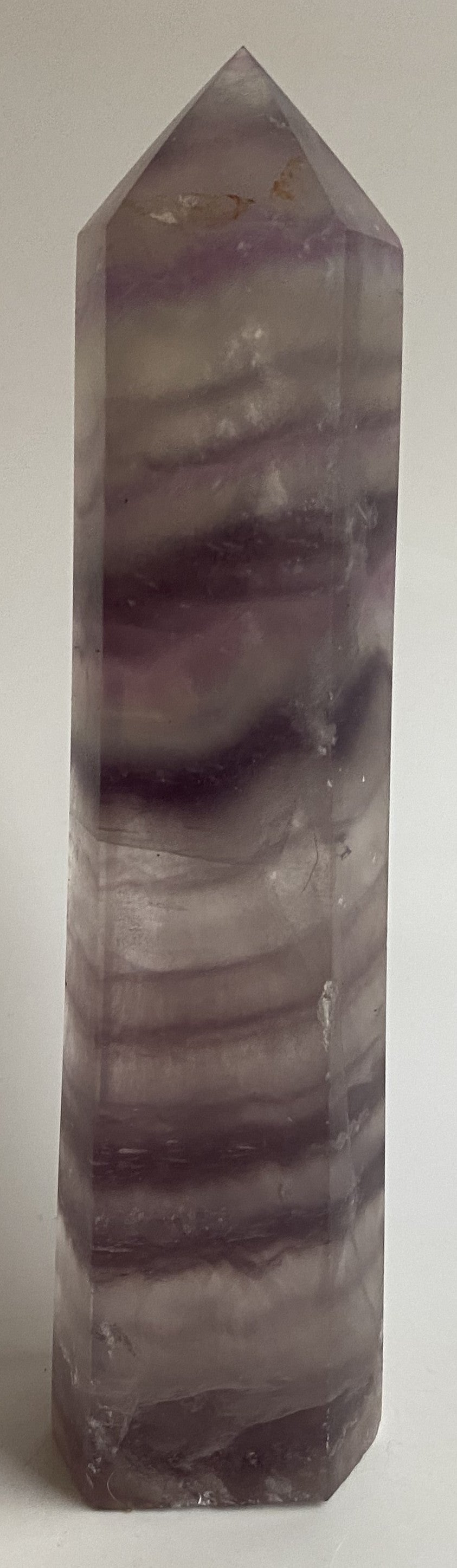 Obelisc din cristal de fluorit mov pe fundal alb sub lumina naturala