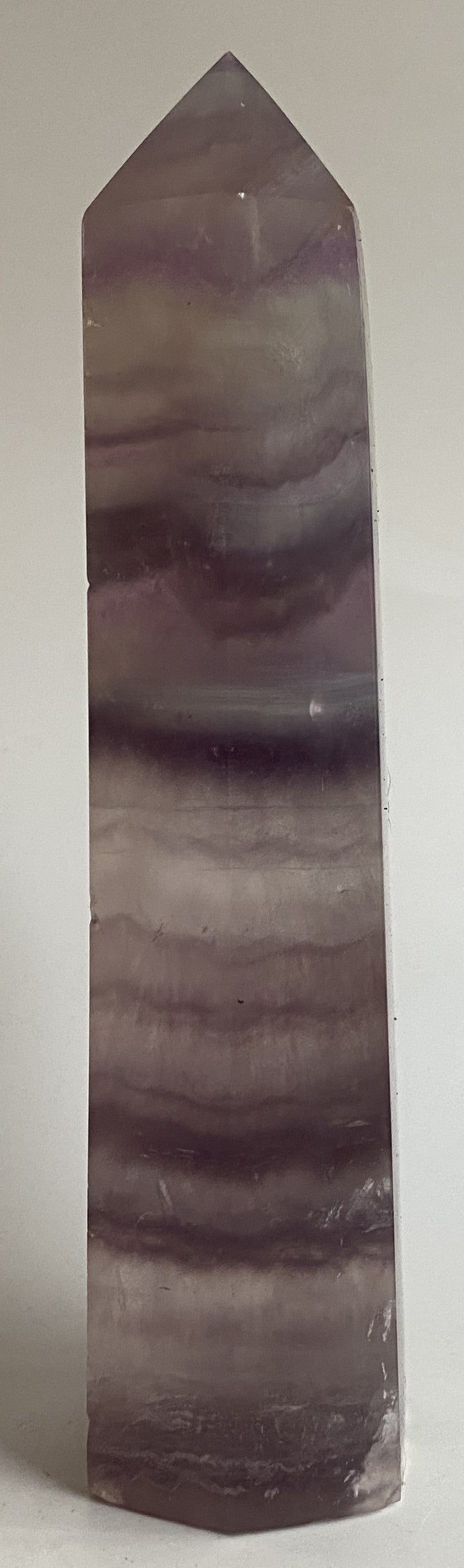 Obelisc din cristal de fluorit mov pe fundal alb sub lumina naturala