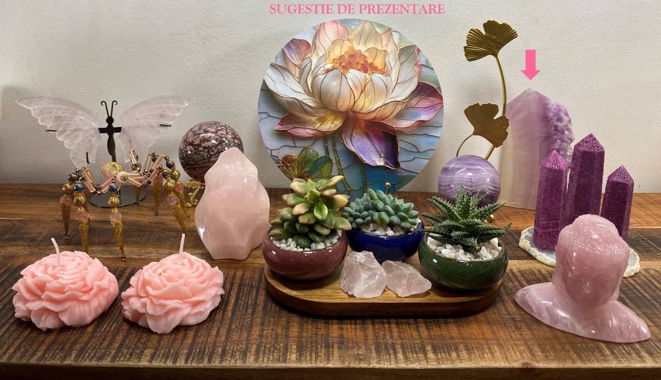 Obelisc brut din piatra semipretioasa Fluorit Silk violet asezat pe masa decorata cu plante si lumanari roz