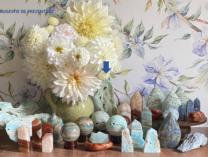 Obelisc brut din Hemimorfit natural de 20cm printre alte pietre semiprețioase lângă buchet de flori albe
