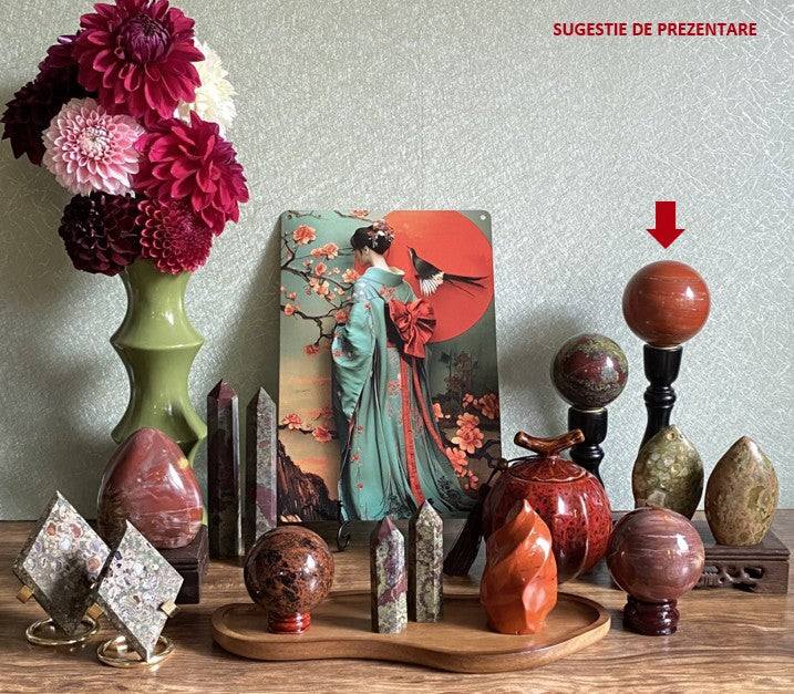 Sfera semipretioasa din Jasp Rosu pe suport metalic, decor si pietre semipretioase diverse pe masa.