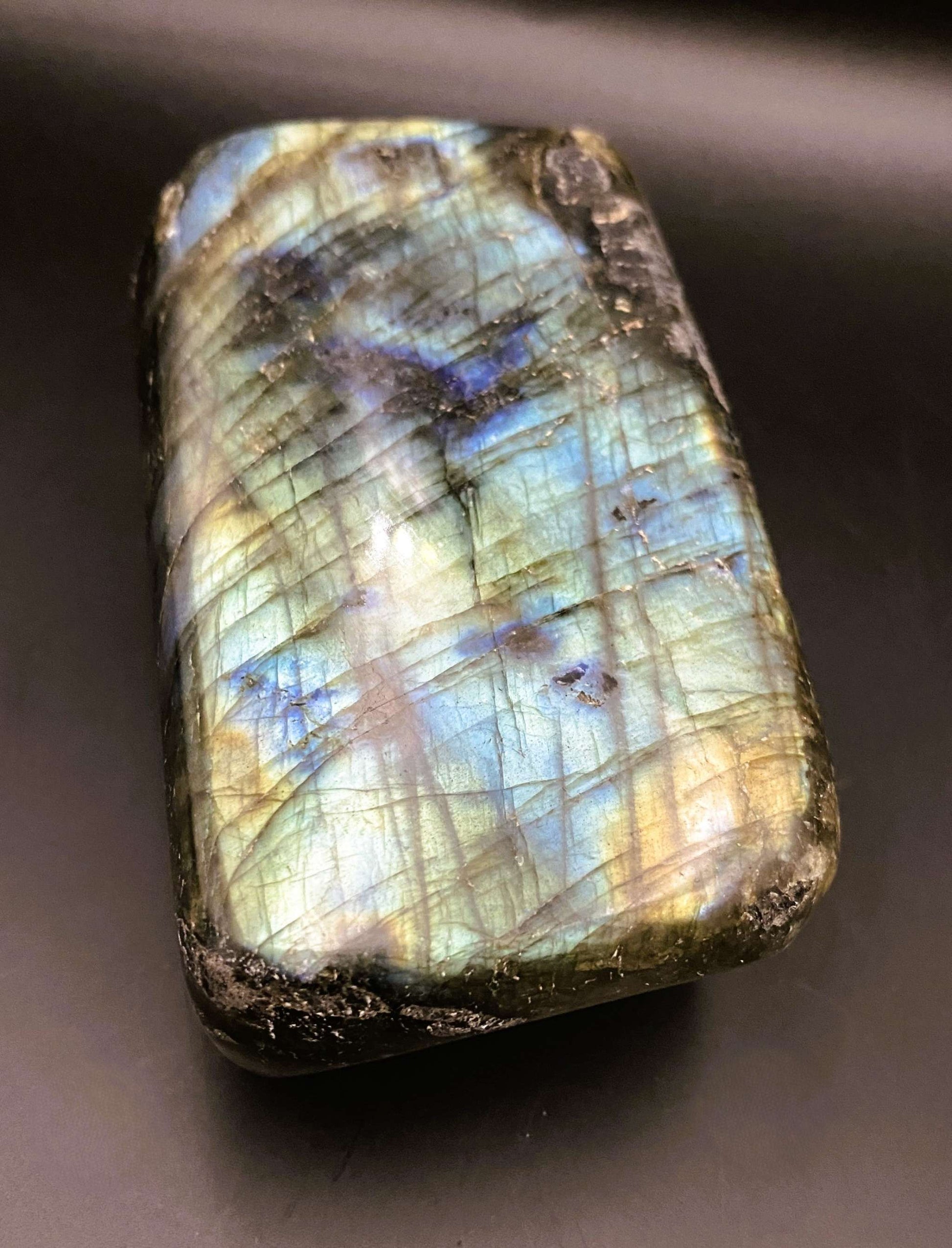 Labradorit sculpted gemstone with iridescent blue and yellow flashes on gray surface under angled light.