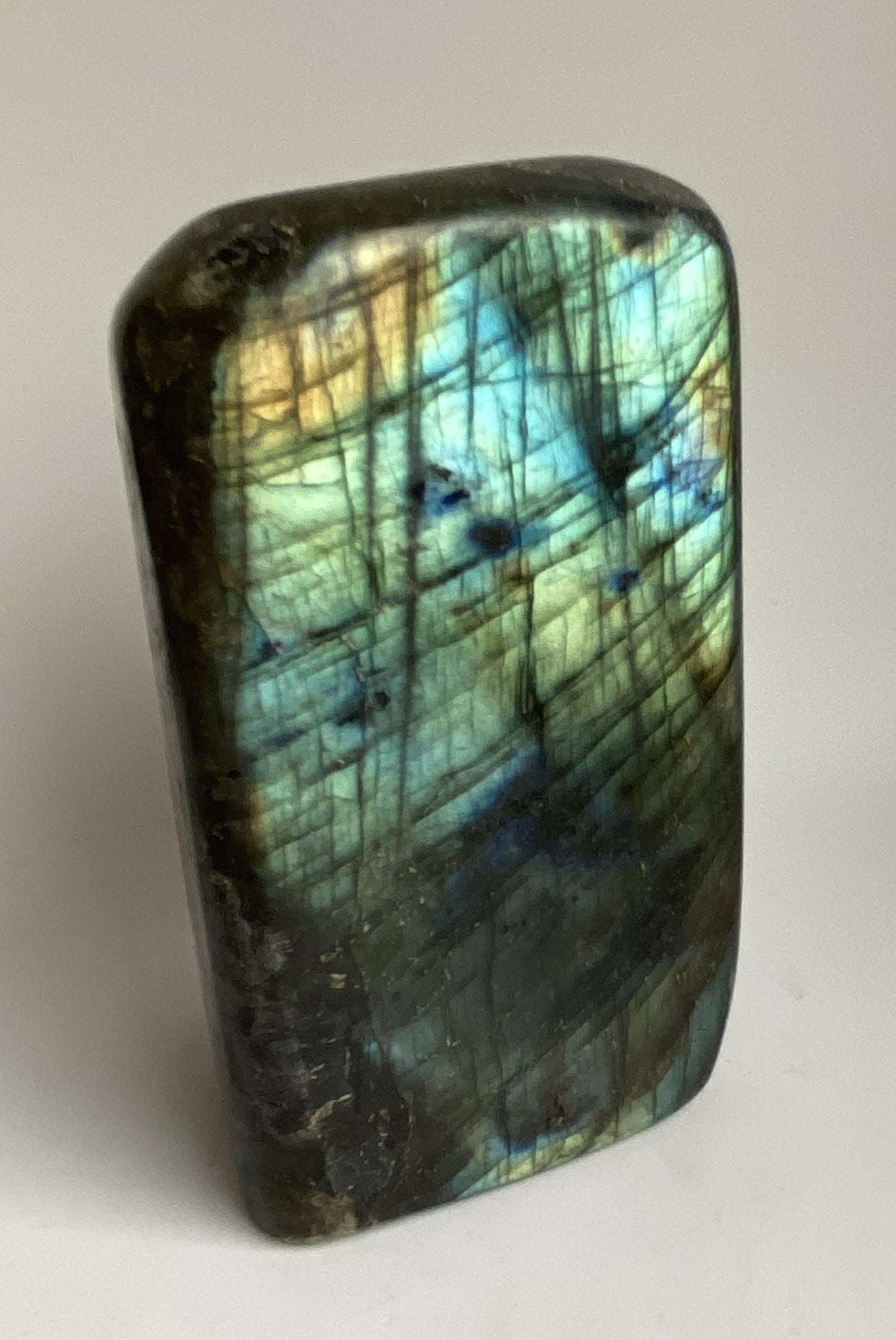 Labradorit semiprecious stone sculpture with blue and yellow iridescence on grey surface