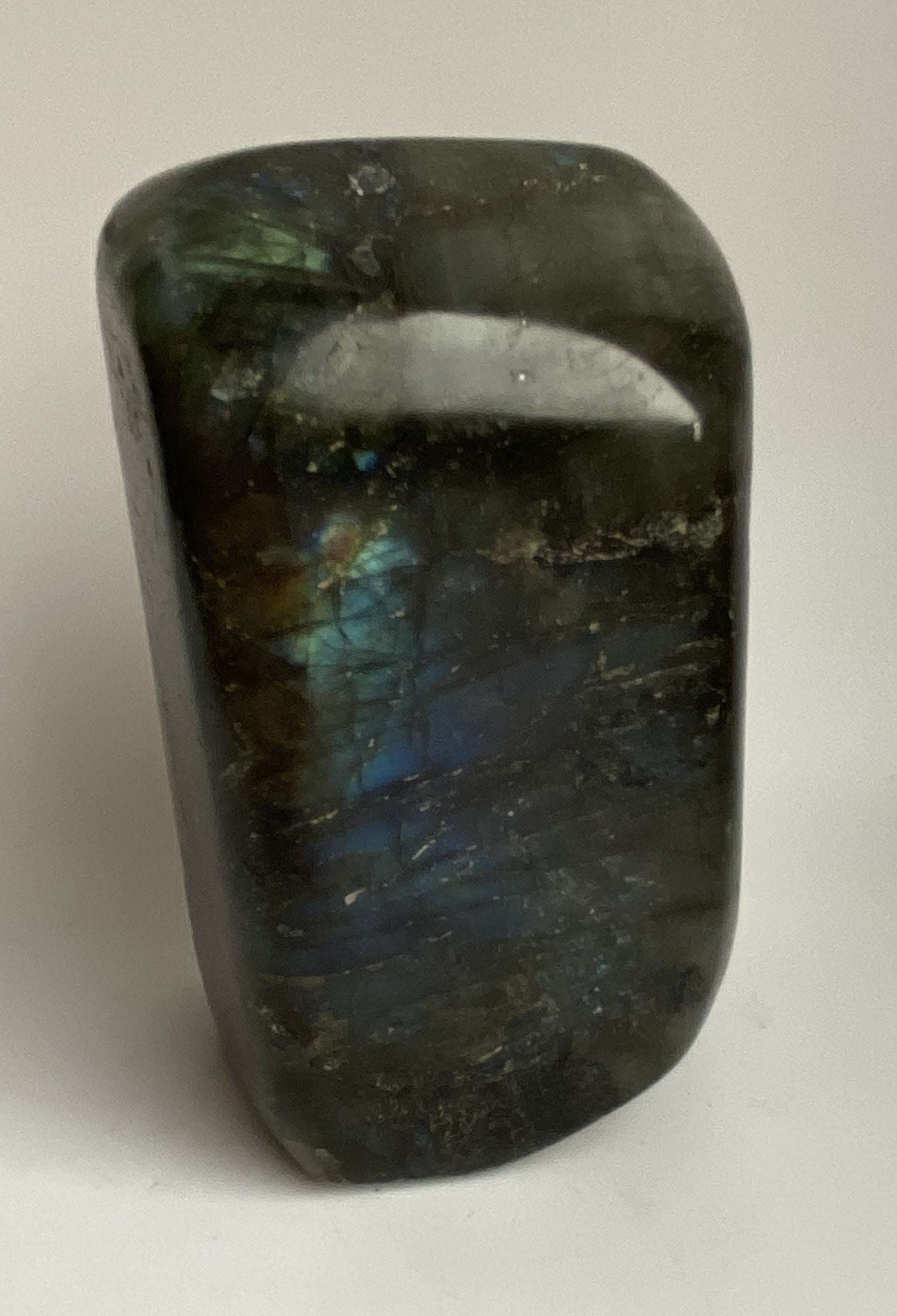Polished Labradorit sculpture with blue and yellow iridescence on gray stone background