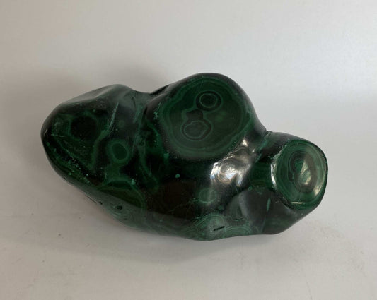 Polished malachite gemstone specimen with green circular patterns on white background