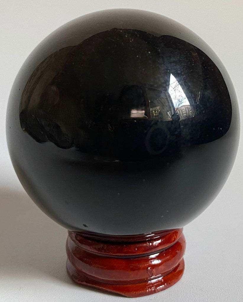Sfera din cristal de obsidian argintiu pe suport din lemn cu fundal negru