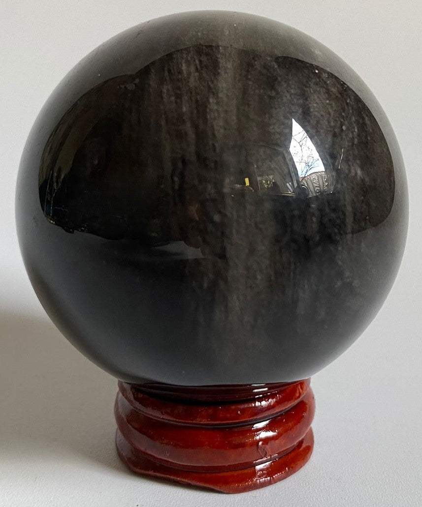 Sfera de 5.4cm din piatra semipretioasa de obsidian argintiu pe suport din lemn cu fundal negru
