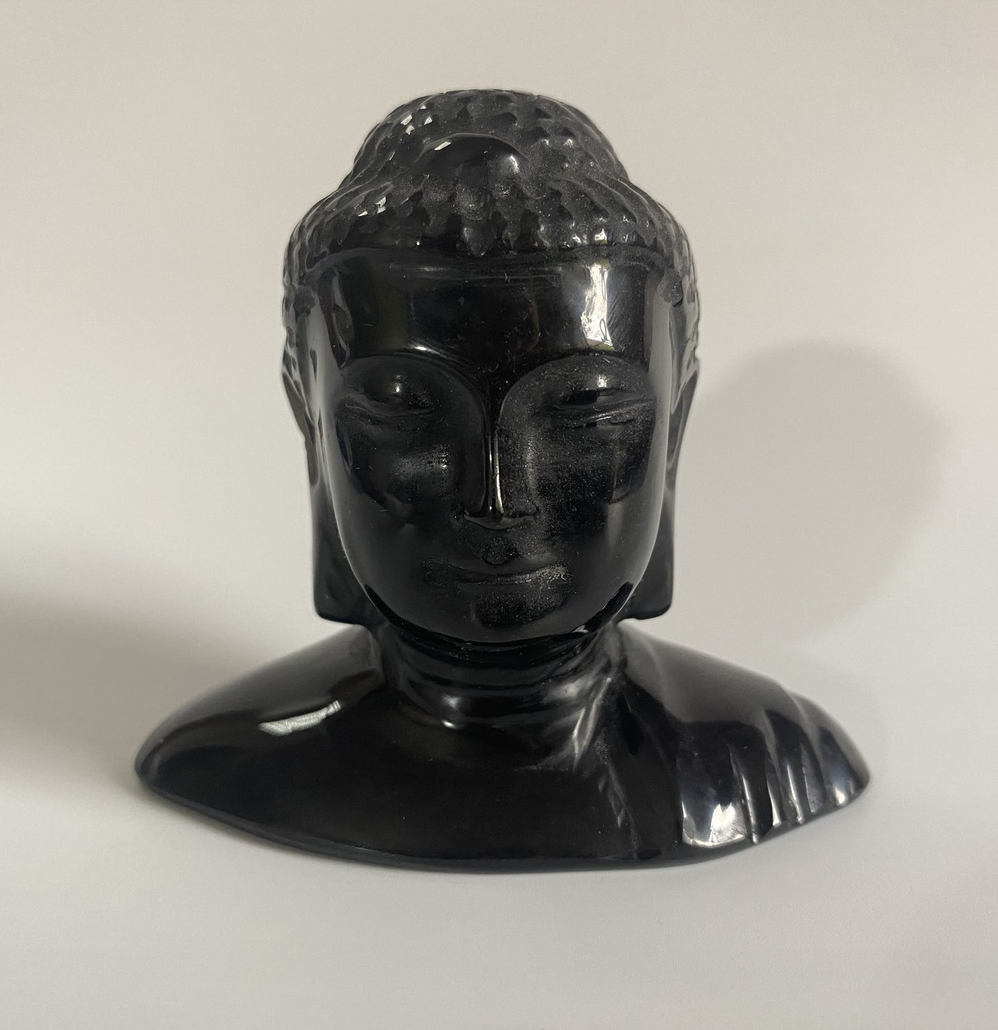 Sculptura cap de Buddha din obsidian negru cu fundal alb sub lumina naturala