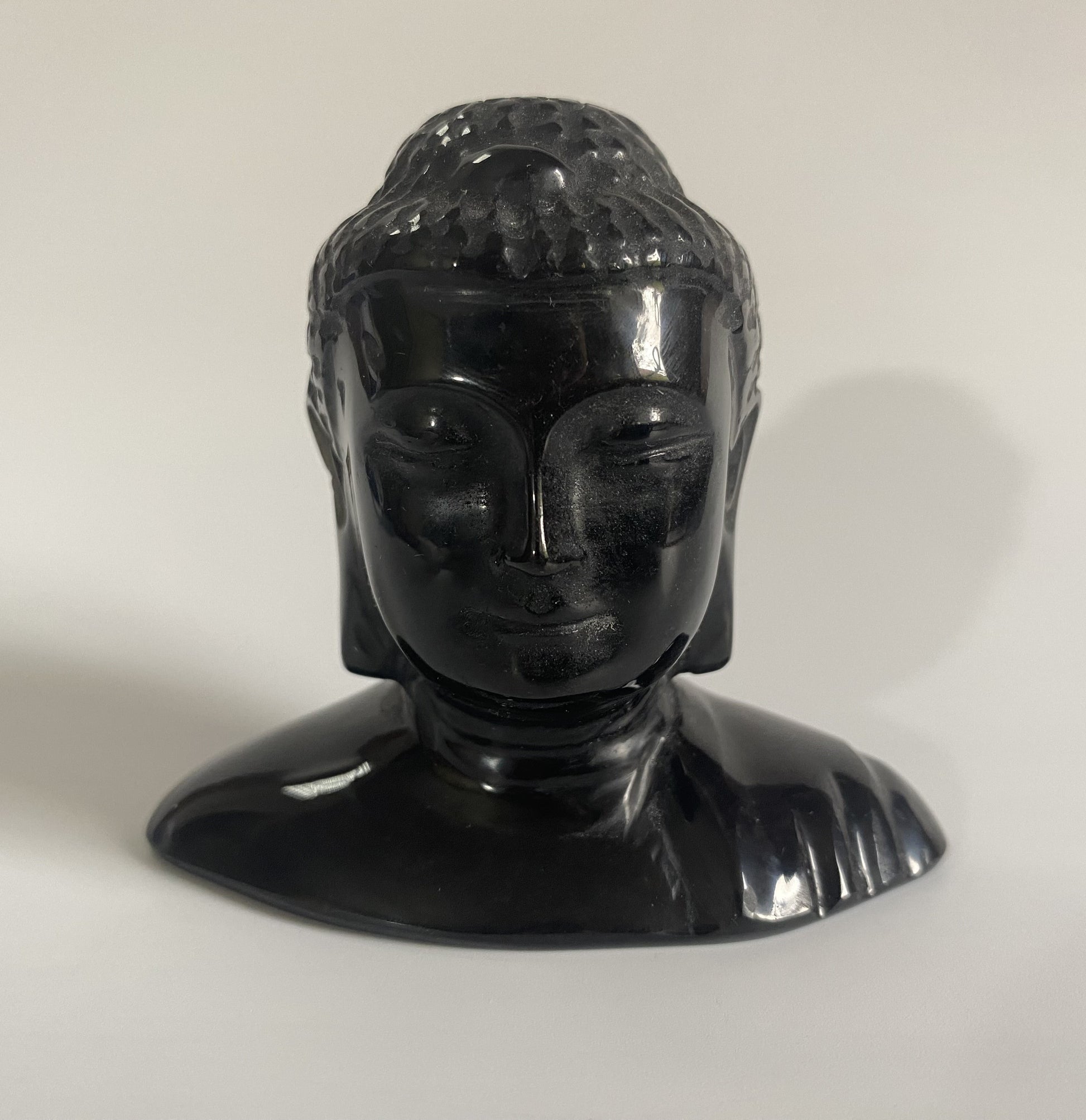 Sculptura cap de Buddha din obsidian negru cu fundal alb sub lumina naturala