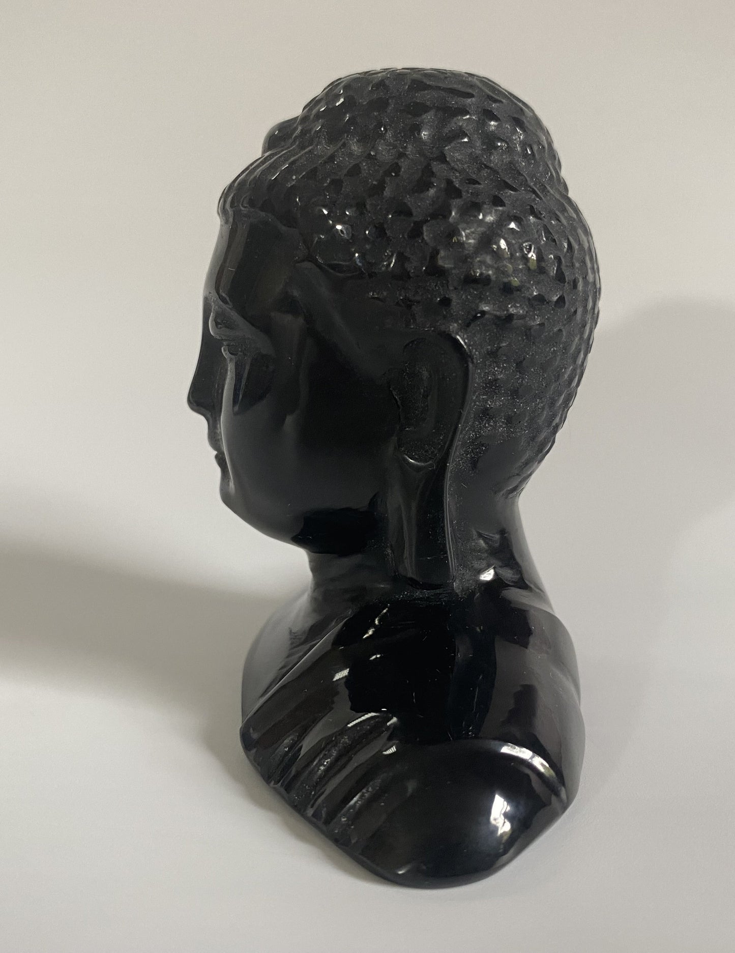 Sculptura cap de Buddha din obsidian negru cu fundal alb sub lumina naturala