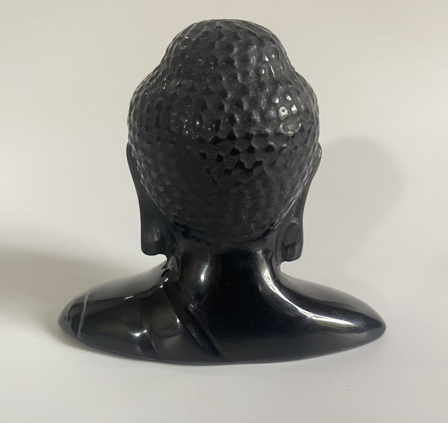 Sculptura cap de Buddha din obsidian negru cu fundal alb sub lumina naturala