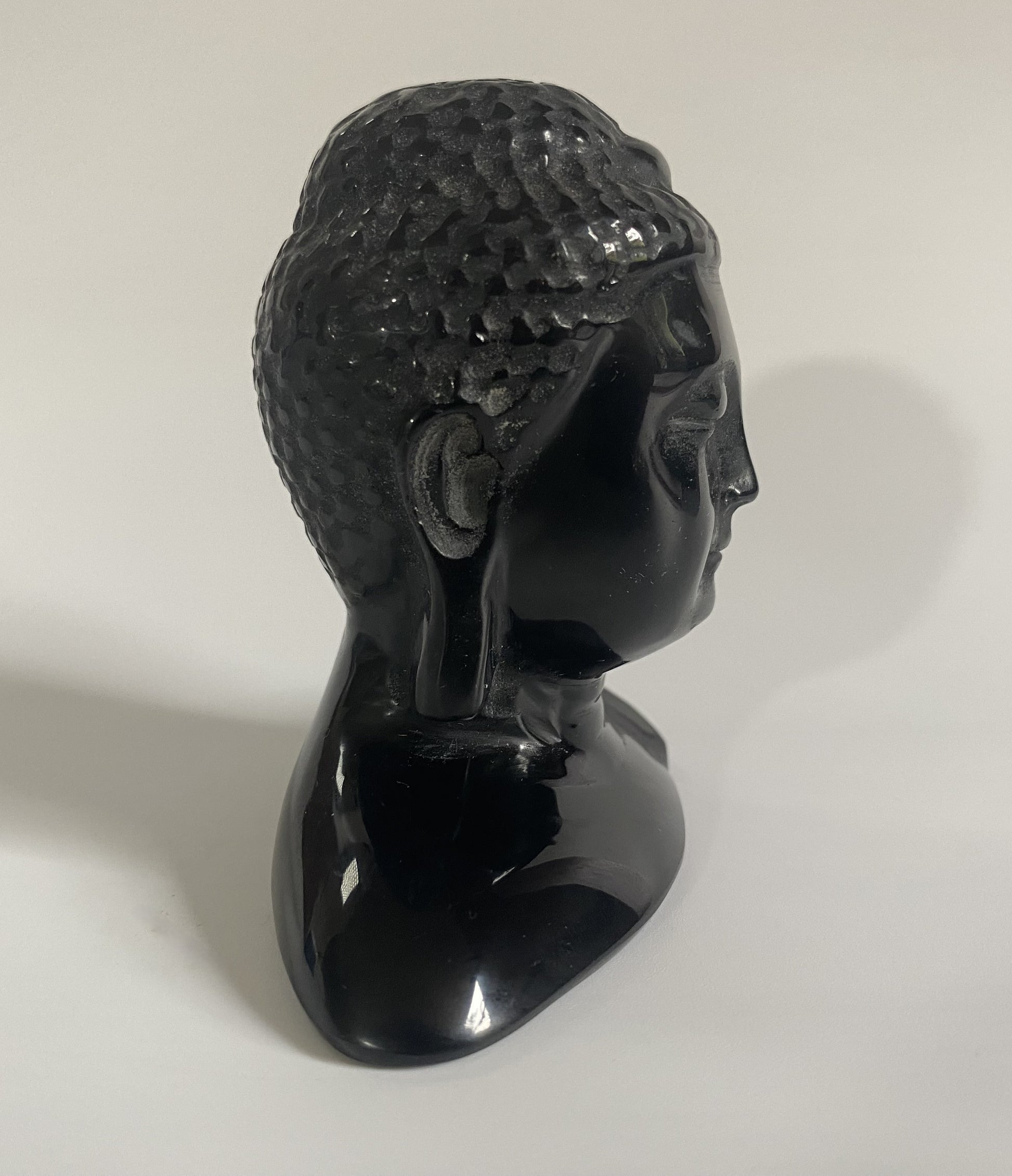 Sculptura cap de Buddha din obsidian negru cu fundal alb sub lumina naturala