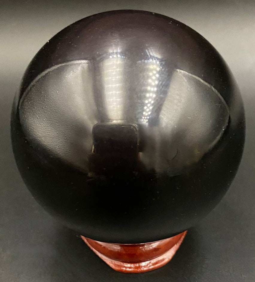 Sfera din piatra semipretioasa de obsidian curcubeu pe suport din lemn cu fundal negru