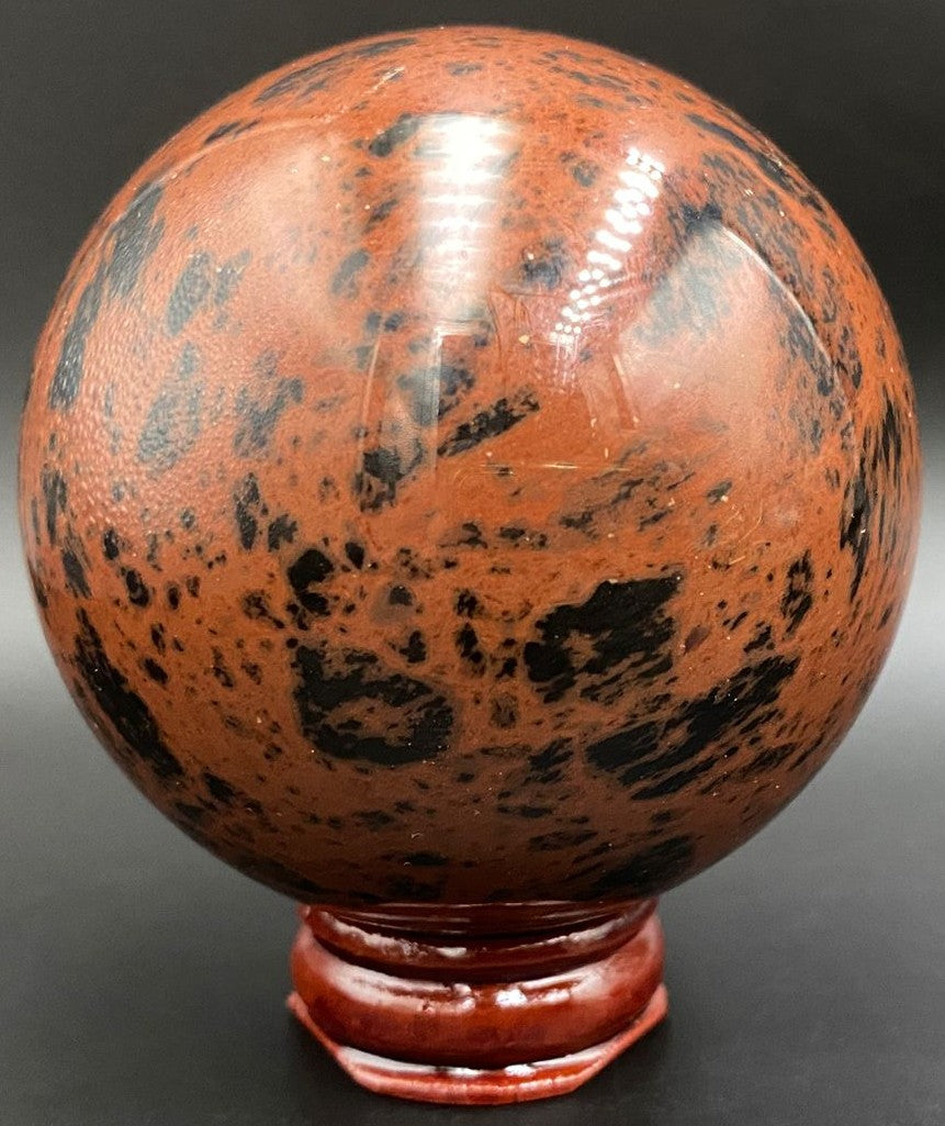 Sfera din piatra semipretioasa de obsidian mahon pe suport din lemn cu fundal negru