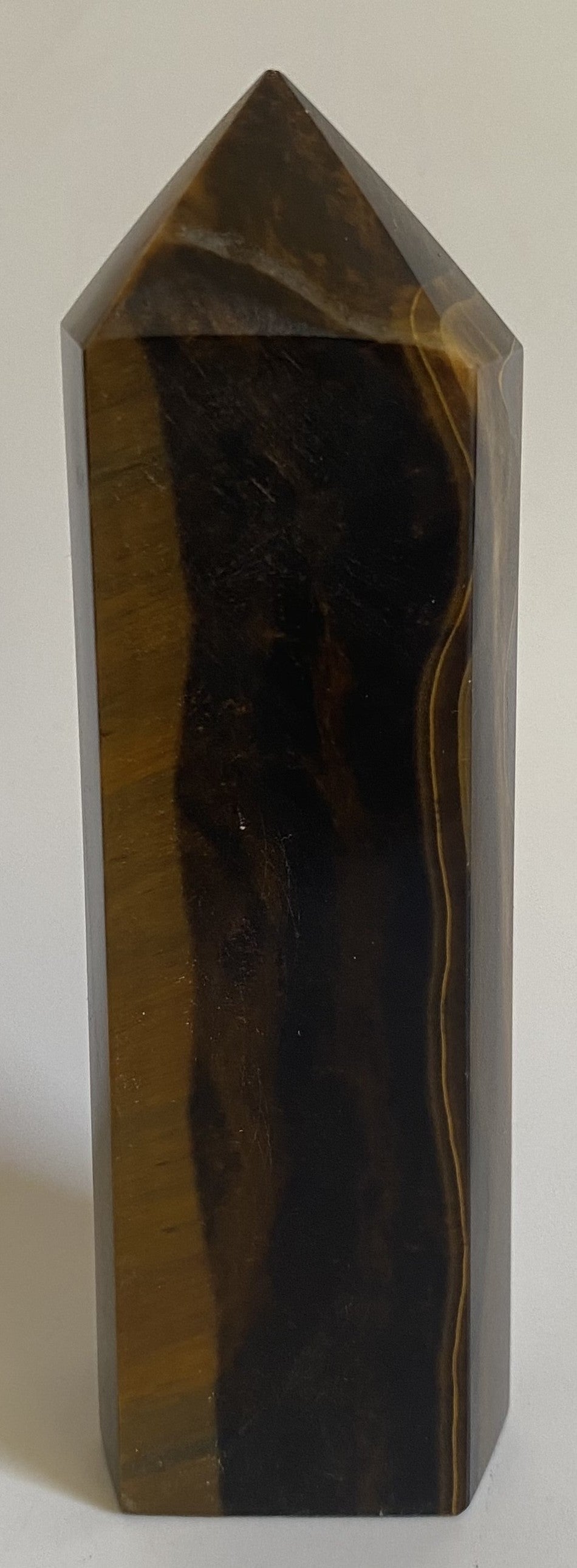 Obelisc din mineral de ochi de tigru pe fundal alb sub lumina naturala