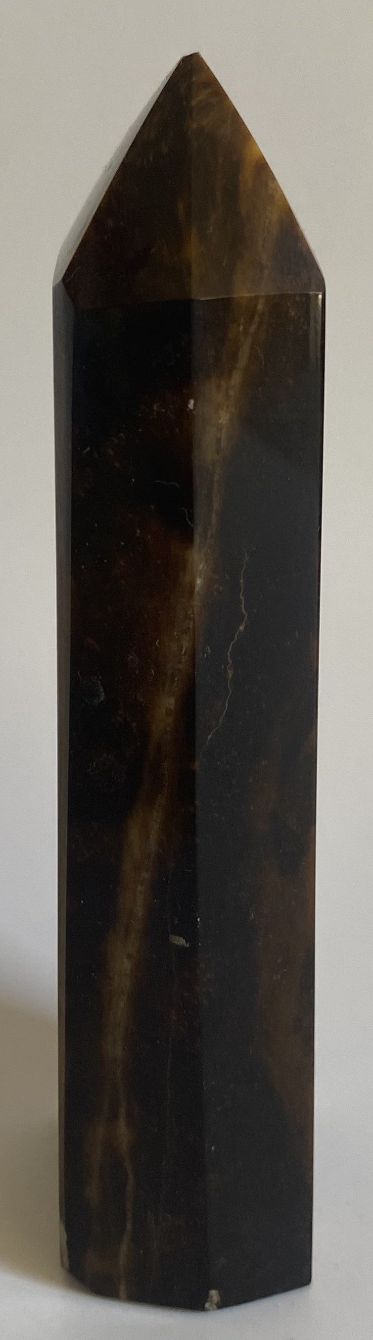 Obelisc din mineral de ochi de tigru pe fundal alb sub lumina naturala