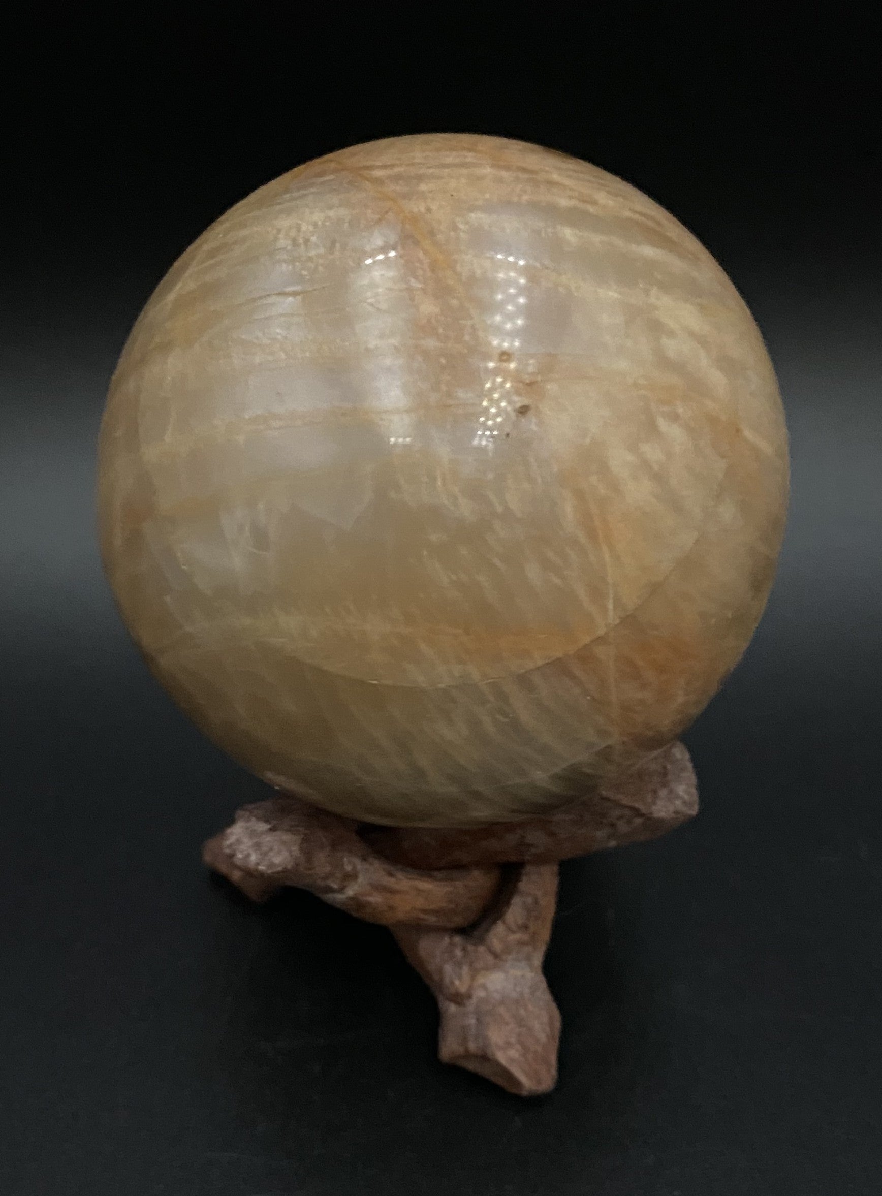 Sfera din mineral de piatra lunii pe suport din lemn, pe fundal negru sub lumina artificiala