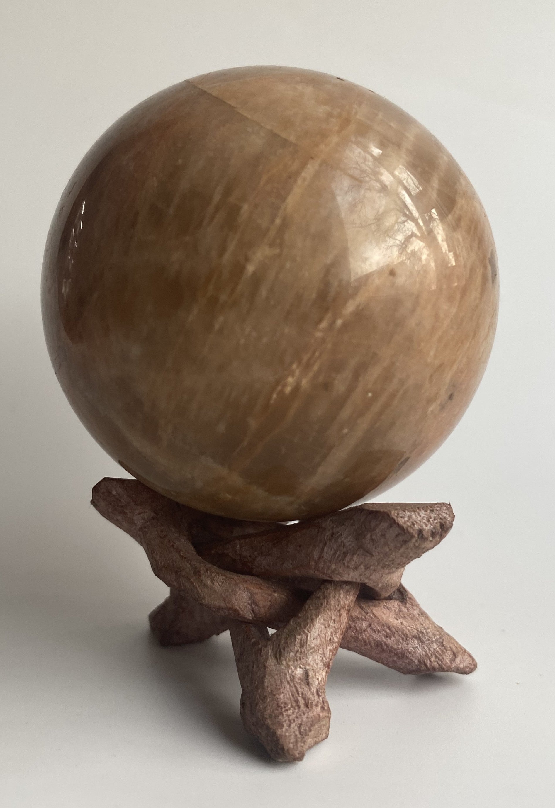Sfera din mineral de piatra lunii pe suport din lemn, pe fundal alb sub lumina naturala