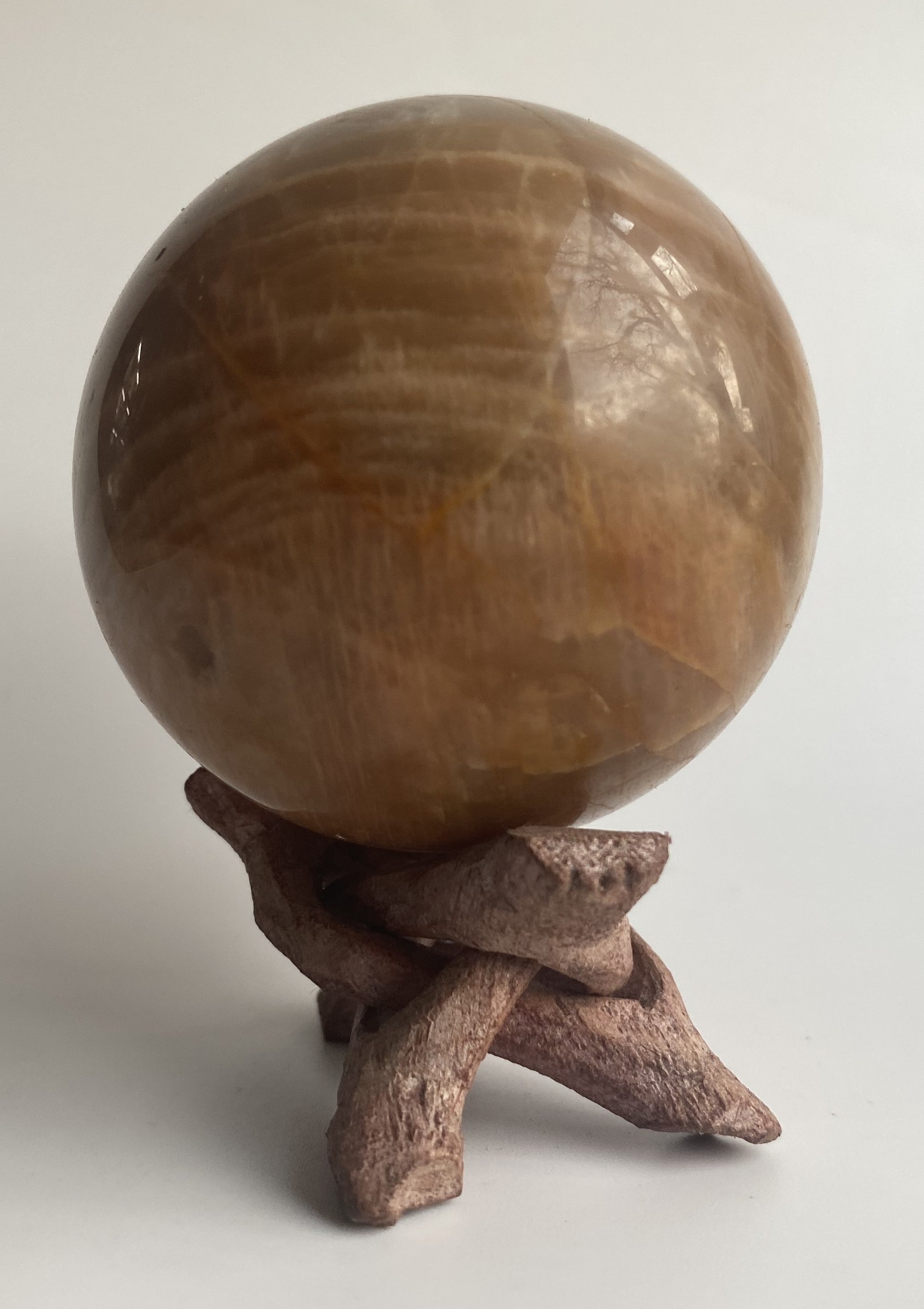 Sfera din mineral de piatra lunii pe suport din lemn, pe fundal alb sub lumina naturala