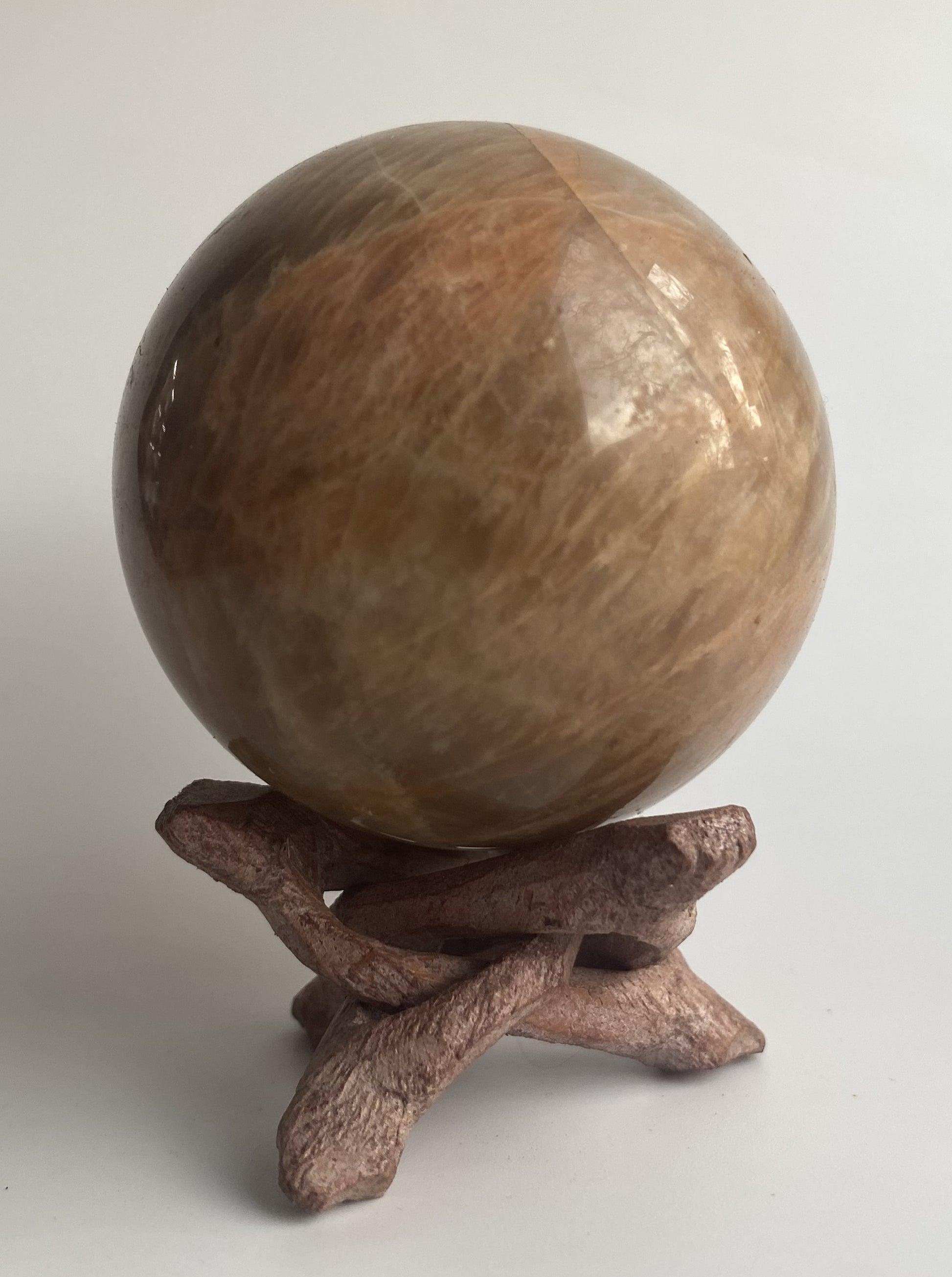 Sfera din mineral de piatra lunii pe suport din lemn, pe fundal alb sub lumina naturala