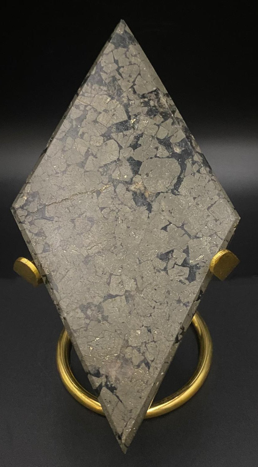 Romb din mineral de pirita cu suport metalic auriu pe fundal negru sub lumina artificiala