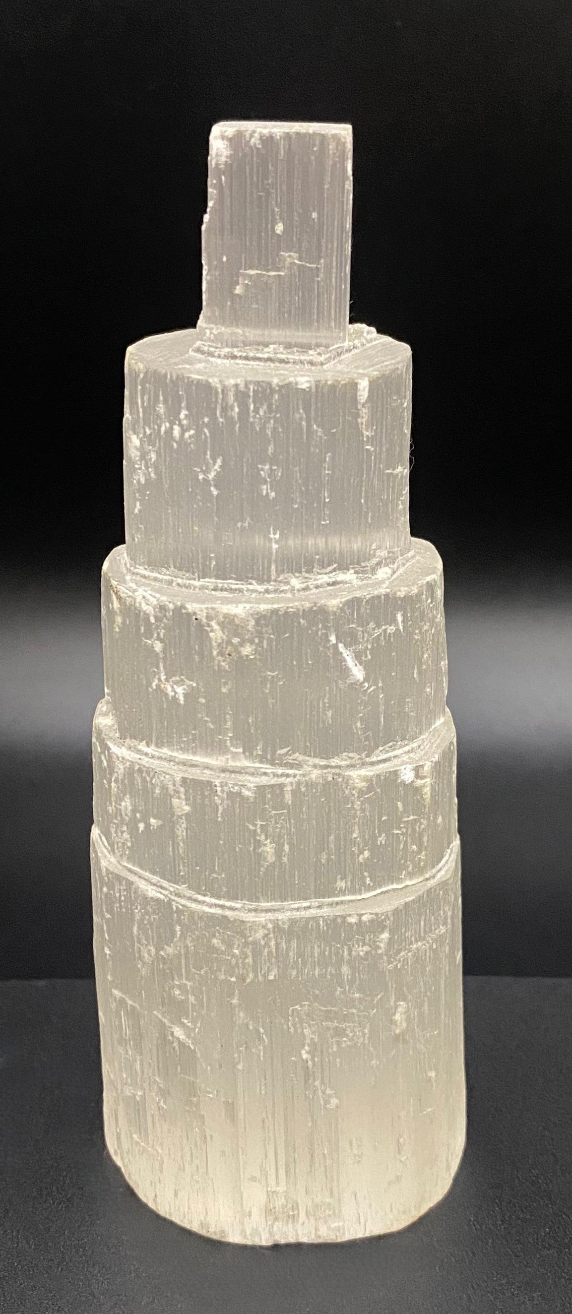 Obelisc turn din mineral de selenit pe fundal negru sub lumina artificiala