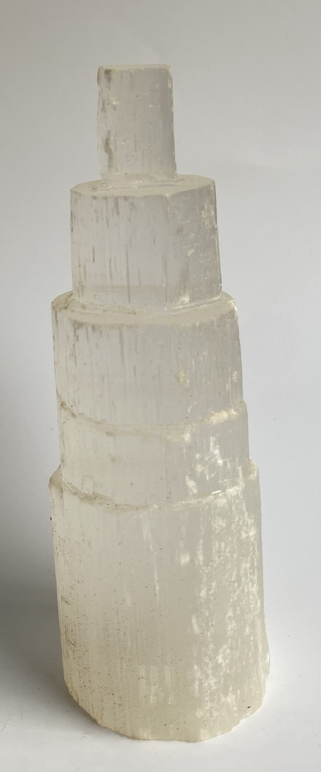 Obelisc turn din mineral de selenit pe fundal alb sub lumina naturala