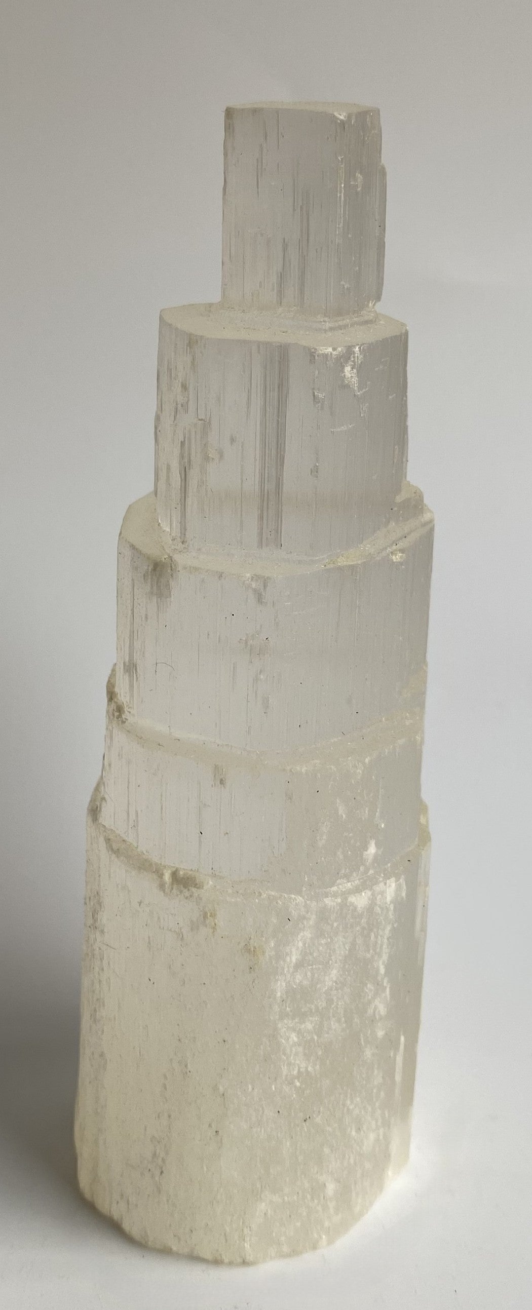 Obelisc turn din mineral de selenit pe fundal alb sub lumina naturala