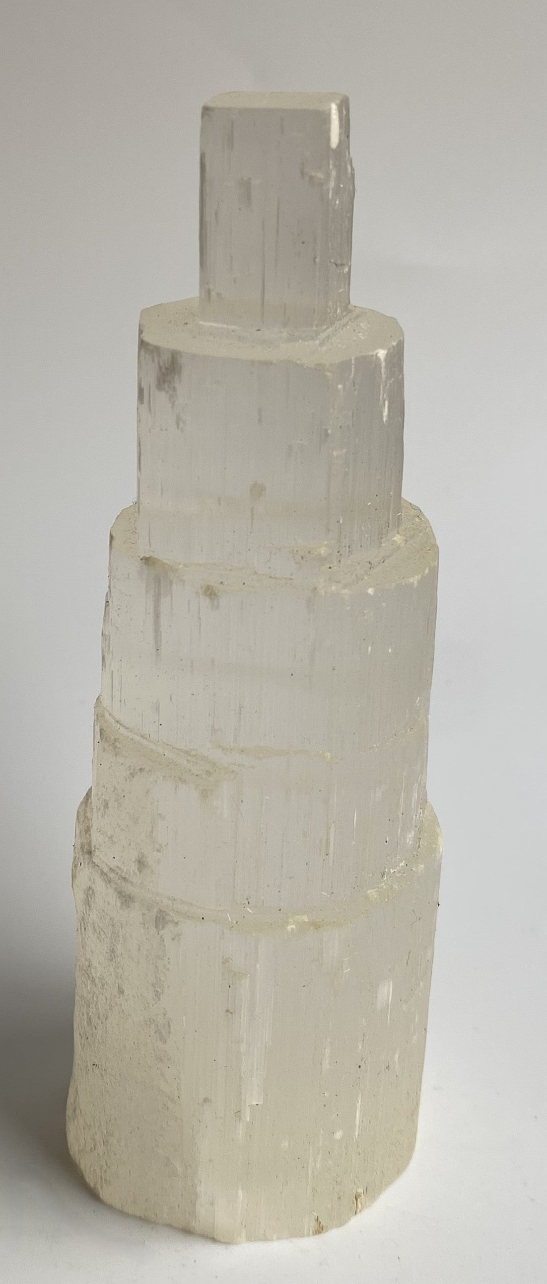 Obelisc turn din mineral de selenit pe fundal alb sub lumina naturala