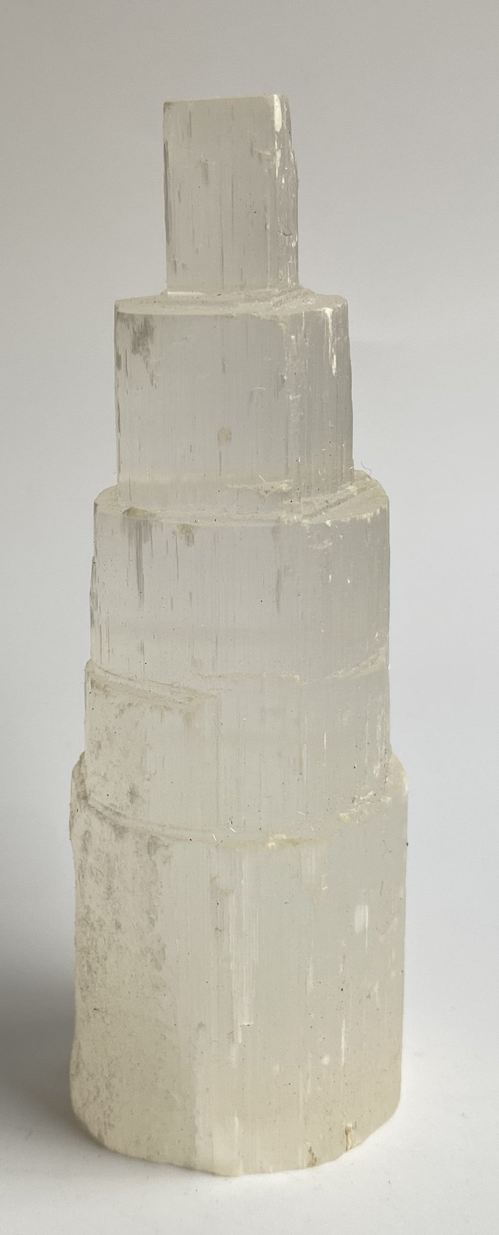 Obelisc turn din mineral de selenit pe fundal alb sub lumina naturala